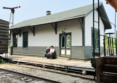 2025-06-09 Waiting for the Next Train, submitted by Jim Ross and showing Jim and Cathie Ross at City Point in Belfast, ME last week waiting for the next train. They may still be there… #waitingforthetrain #checkthe schedule #spendingtimetogether #trainstation #decommissionedstation #belfastmaine #baysidemaine