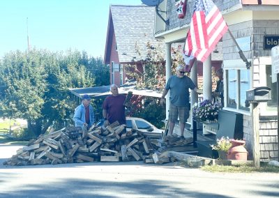 2025-09-22 Wood Pile(Up), photographed by Kathleen Kearns as summer turns to fall in Bayside, ME. Gordon Fuller, Drexell White, and an unidentified helper (on the left) individually inspected and then passed along split wood to Beanie Einstein. It looks like the process might have taken quite a while. No word on what was done with any rejected pieces. #bucketbrigade #woodpile #splitwood #communityservice #nosweat #keepingwarm #summerturnstofall #rugglespark #baysidemaine